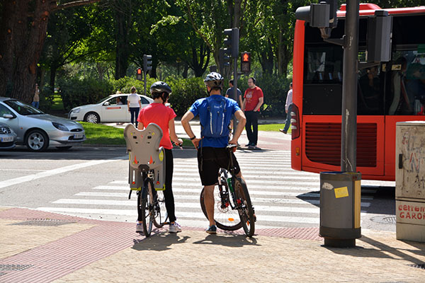 Two bicyclists are waiting at a crosswalk positioned at a curb cut providing a smooth transition from the sidewalk to the street.